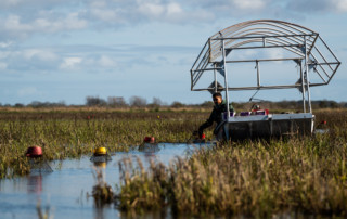 A farm worker picks up a trap while steering his boat through a narrow channel