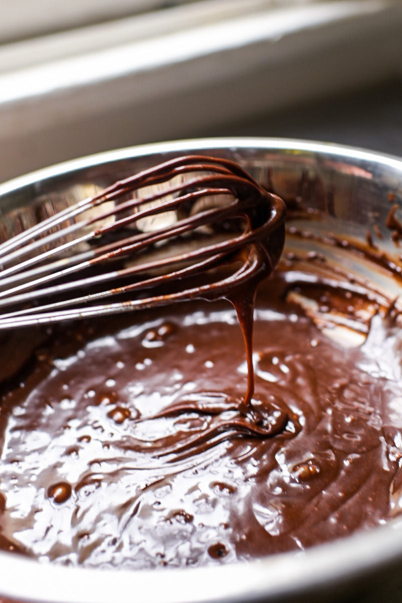 A whisk drips with ganache for homemade brownies
