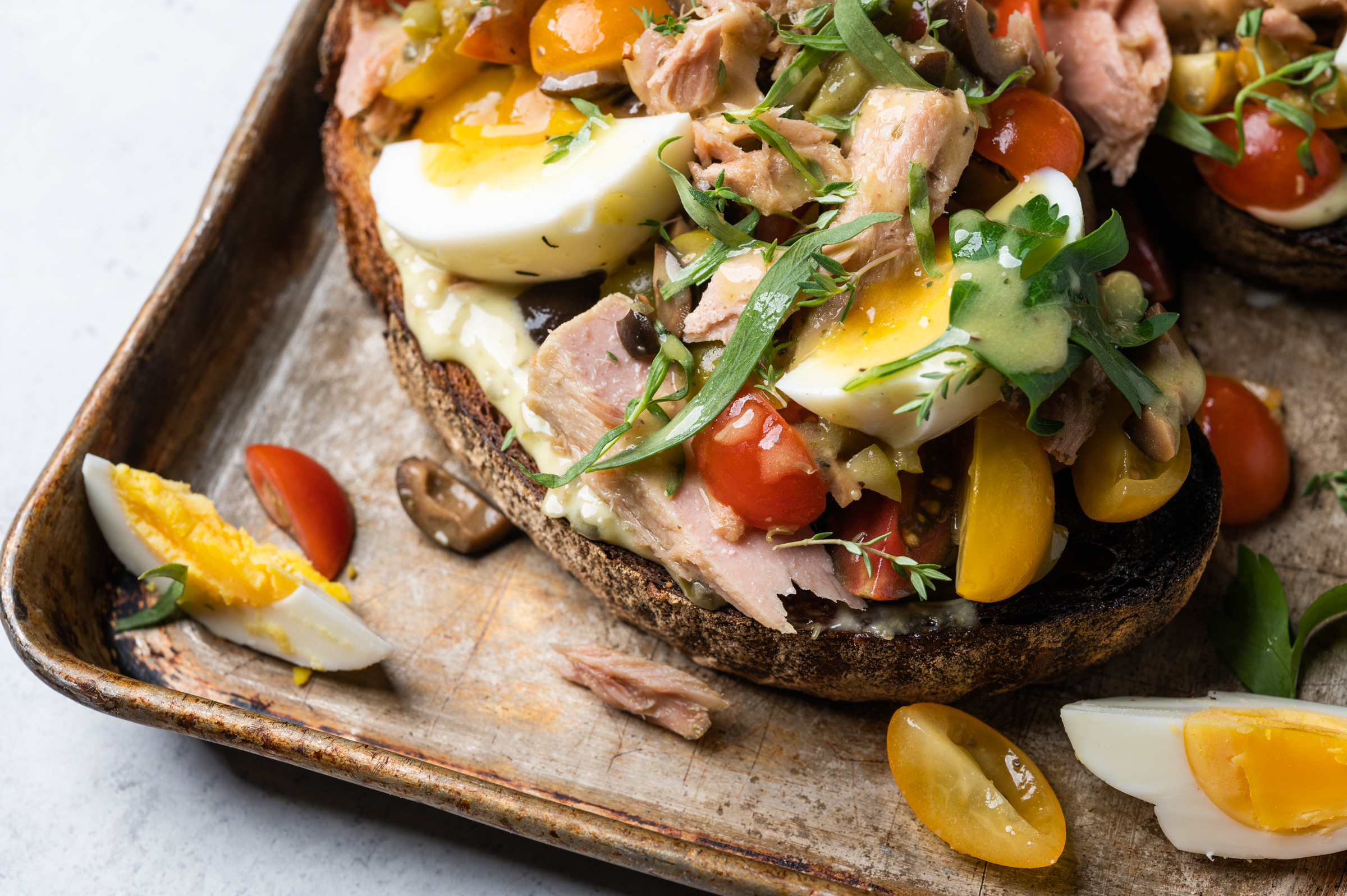 Niçoise toast piled with tomatoes, capers, olives, egg and tuna