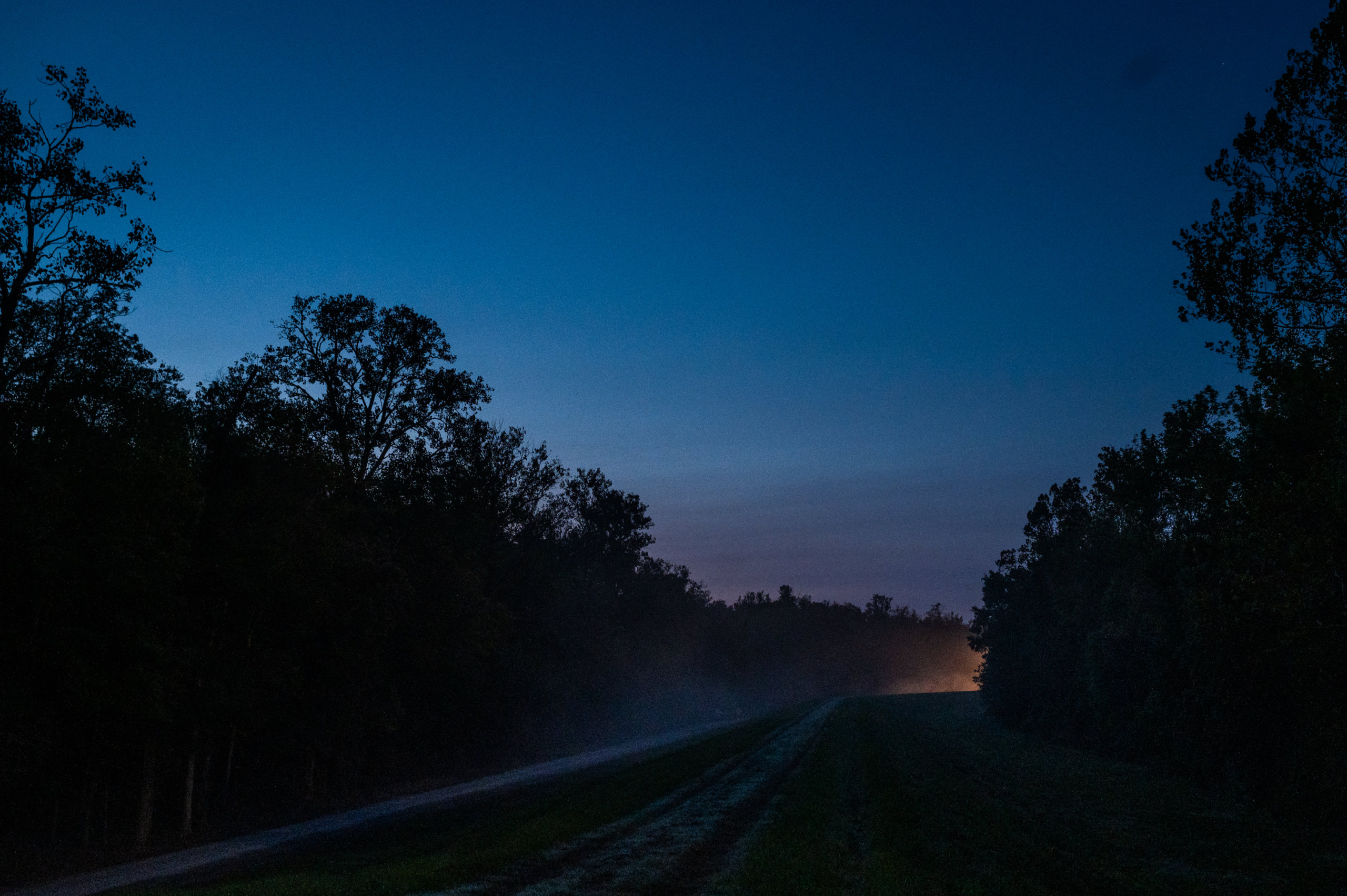 Headlights in the distance shine on a gravel road before sunrise