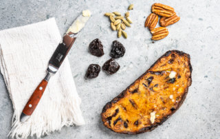 A butter knife next to toasted bread, California prunes, pecans and cardamom pods