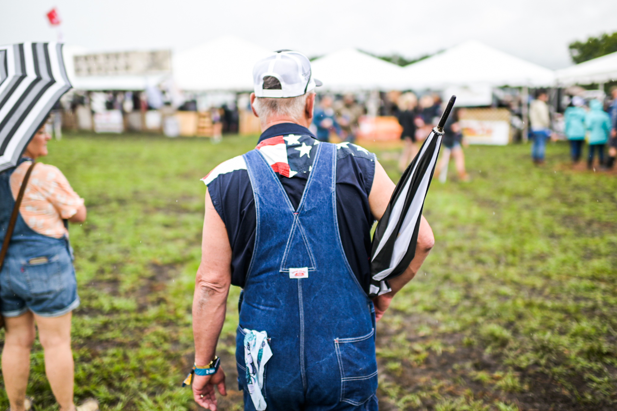 A festival-goer with an umbrella, dressed in overalls and Americana