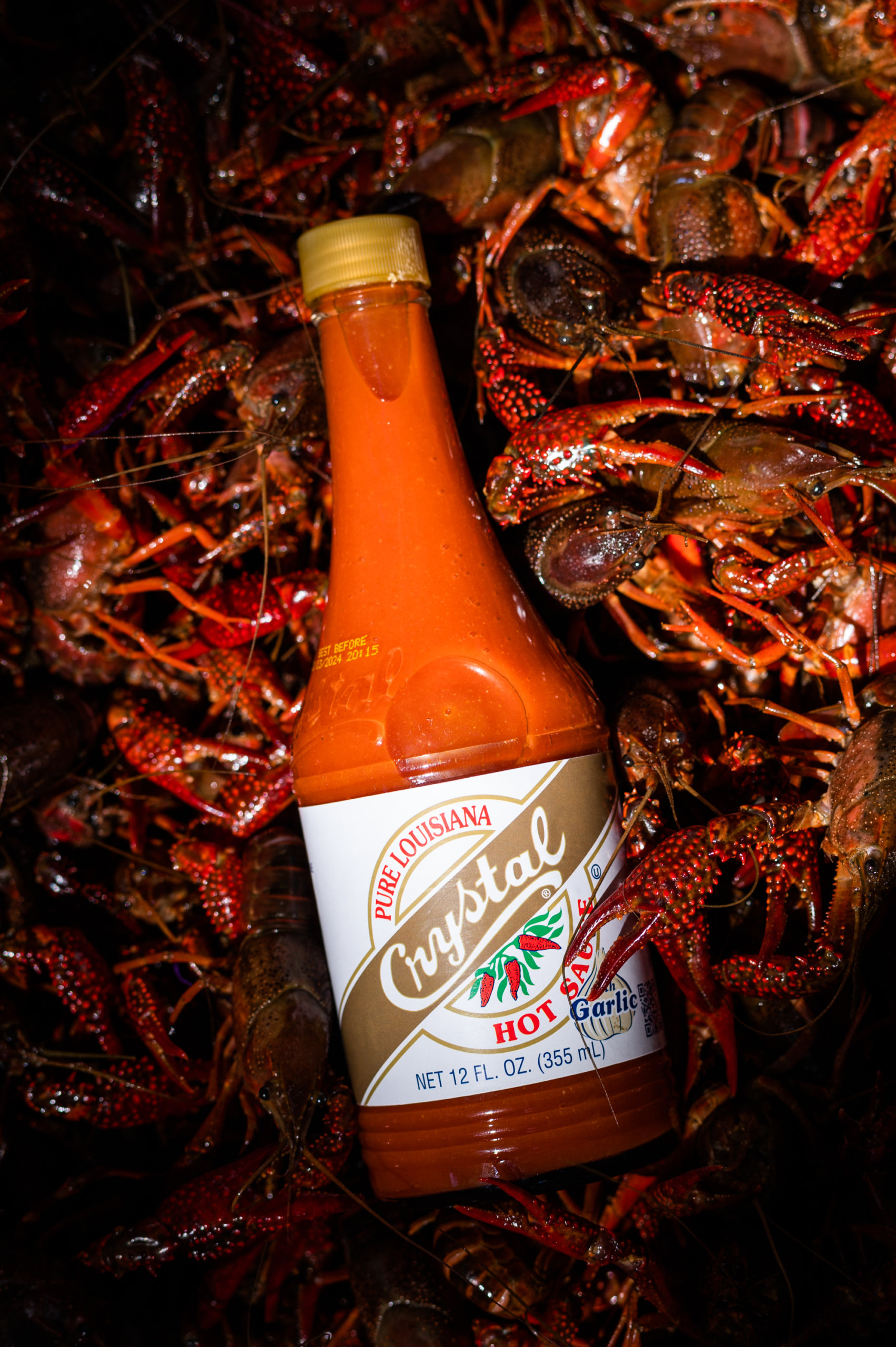 A bottle of Garlic Crystal Hot Sauce on top of live crawfish