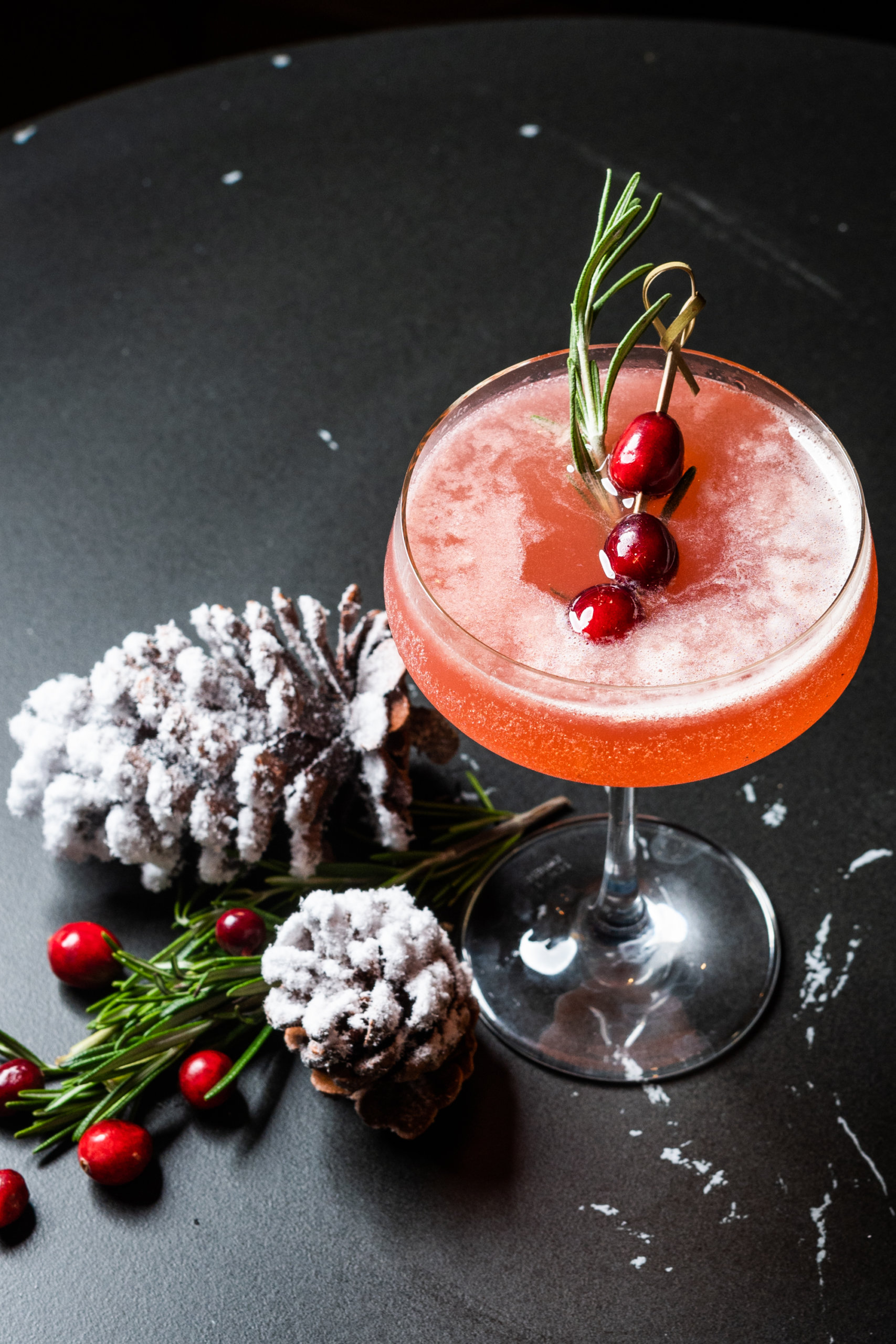 A cocktail garnished with rosemary and cranberries