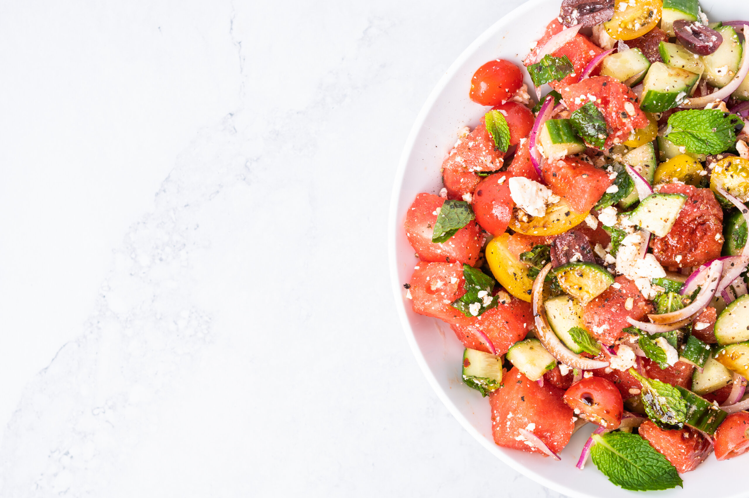 A bowl of watermelon and tomato salad on a marble counter