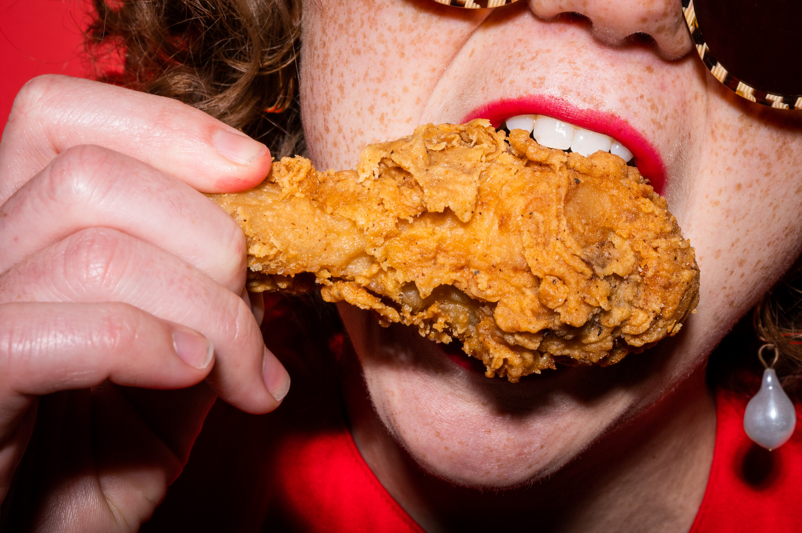 A woman with red lipstick bites into a fried chicken drumstick
