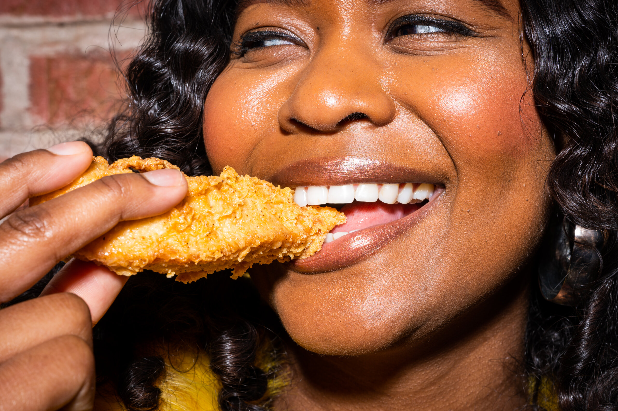 A woman smiles while biting into a chicken tender
