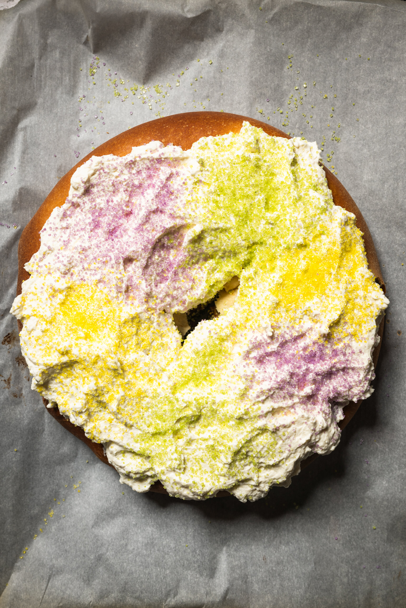 The finished king cake with whipped mascarpone topping decorated with purple, green, and yellow sanding sugars