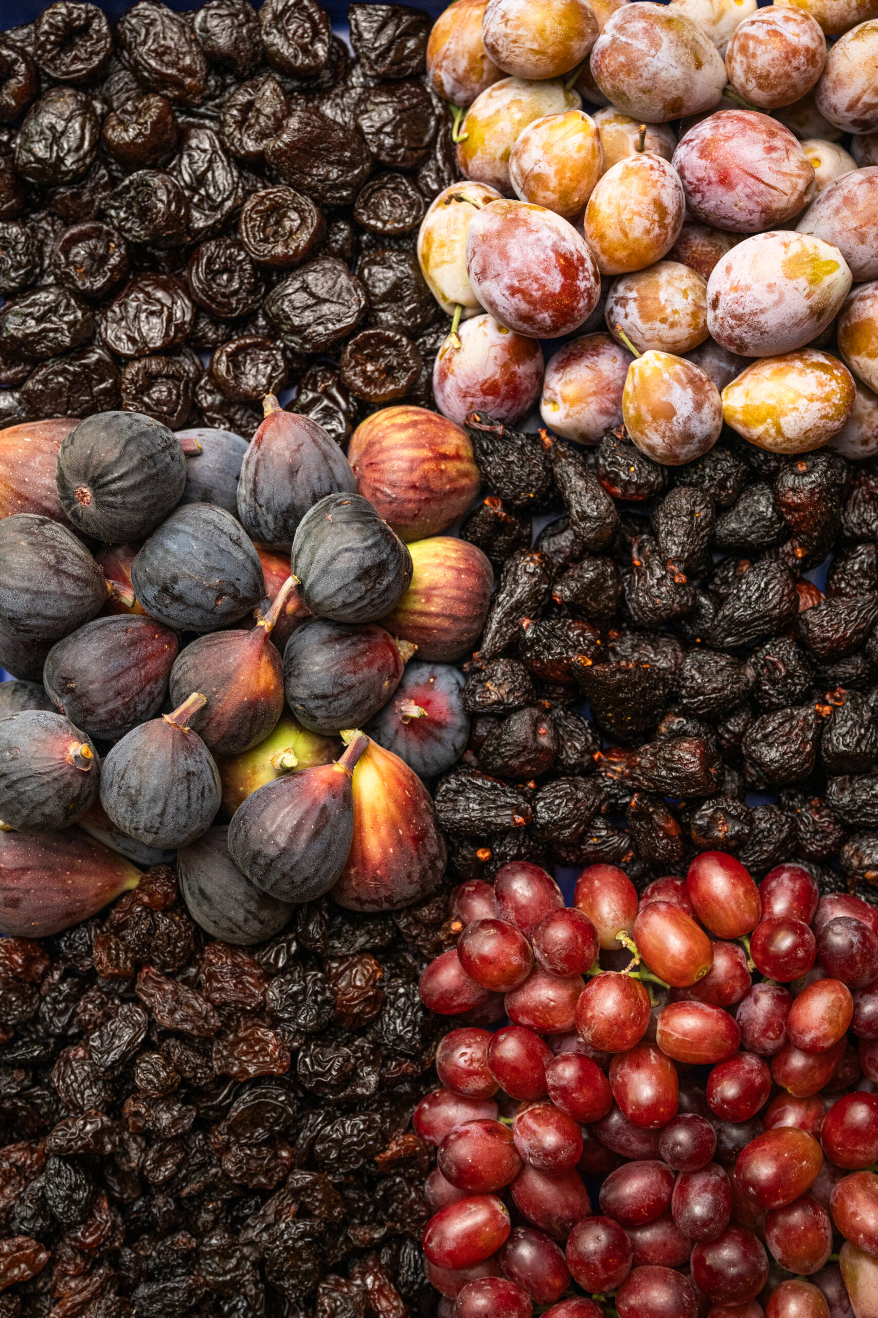 Overhead view of fresh and dried fruit pairings: Prunes, figs, and raisins/grapes.