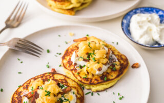 A plate with garnished savory ricotta pancakes in front of a plate filled with all the toppings.