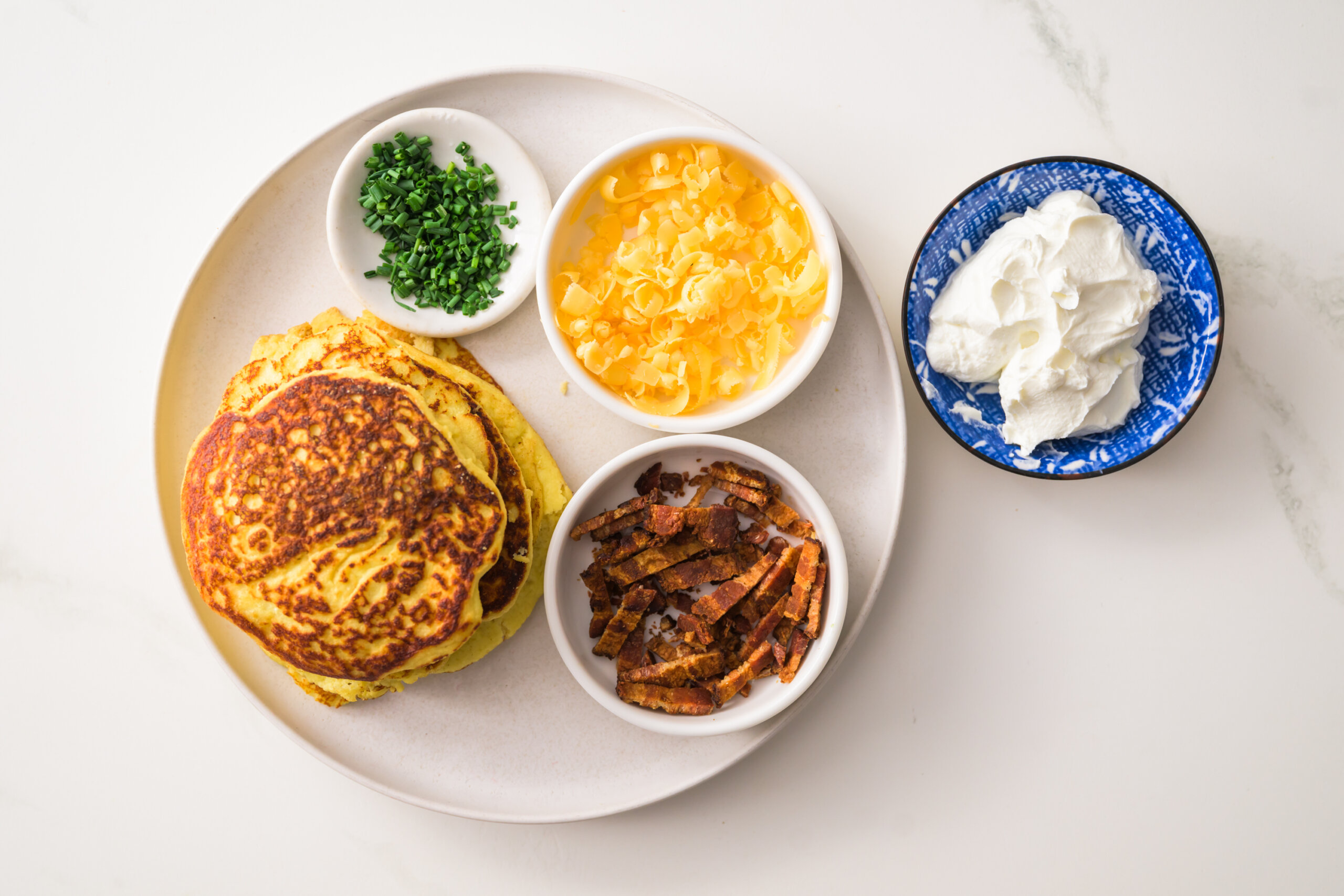 A stack of keto ricotta pancakes with chopped chives, bacon bits, lebneh, and shredded cheddar cheese