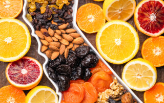 A platter with assorted nuts and dried fruits is surrounded by sliced citrus fruits, including oranges, lemons, and grapefruits, arranged on a wooden surface.