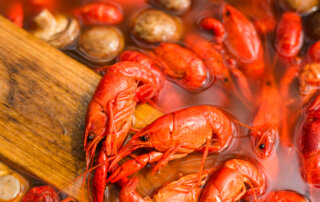 Boiling pot filled with red crawfish and mushrooms, stirred with a wooden paddle.