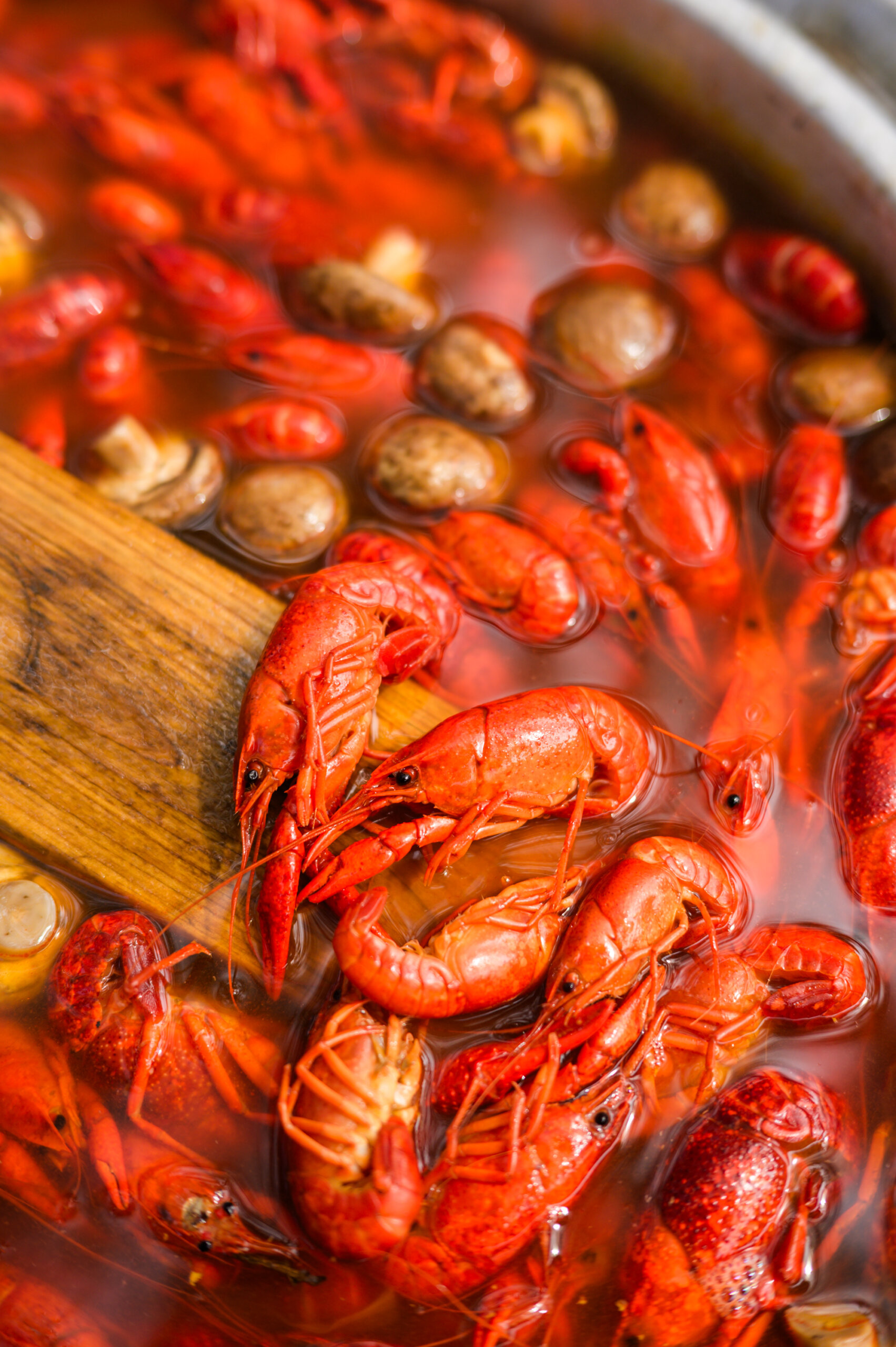 Boiling pot filled with red crawfish and mushrooms, stirred with a wooden paddle.