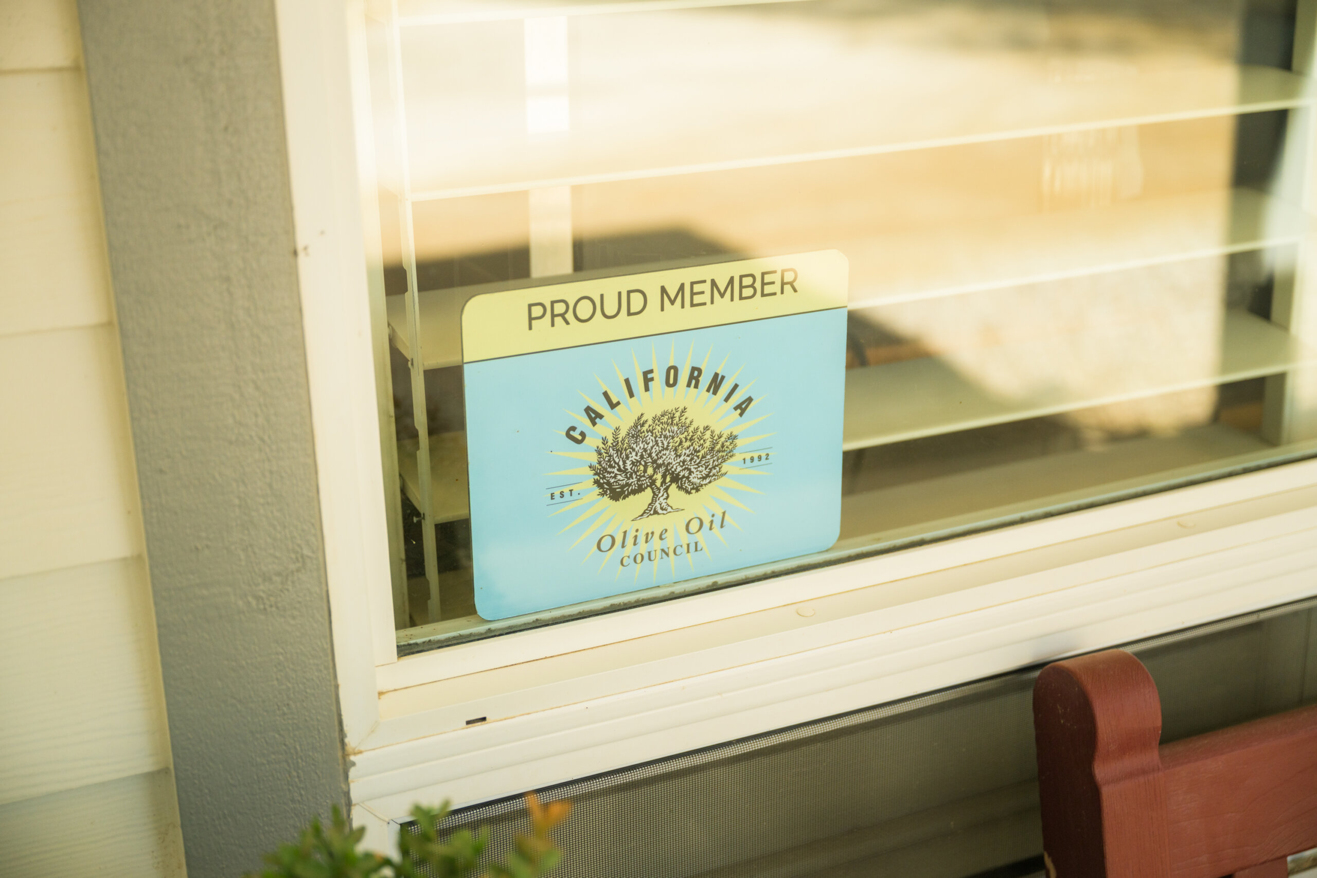 A sign in a window reads "Proud Member" and "California Olive Oil Council" with an olive tree illustration.