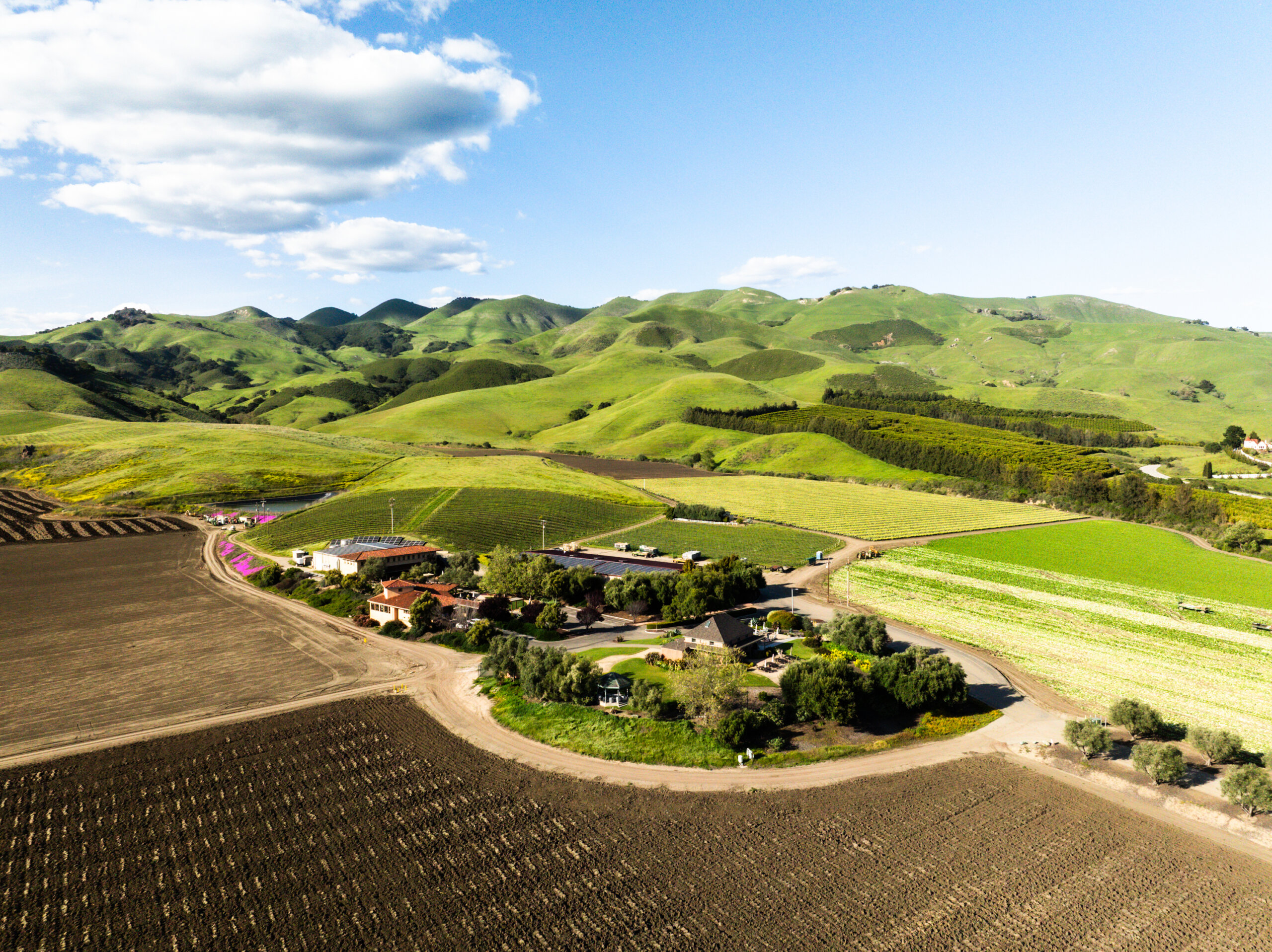Aerial view of a rural landscape with green rolling hills, farmland, scattered houses, and a clear blue sky. Aerial view of a rural landscape with green rolling hills, farmland, scattered houses, and a clear blue sky.