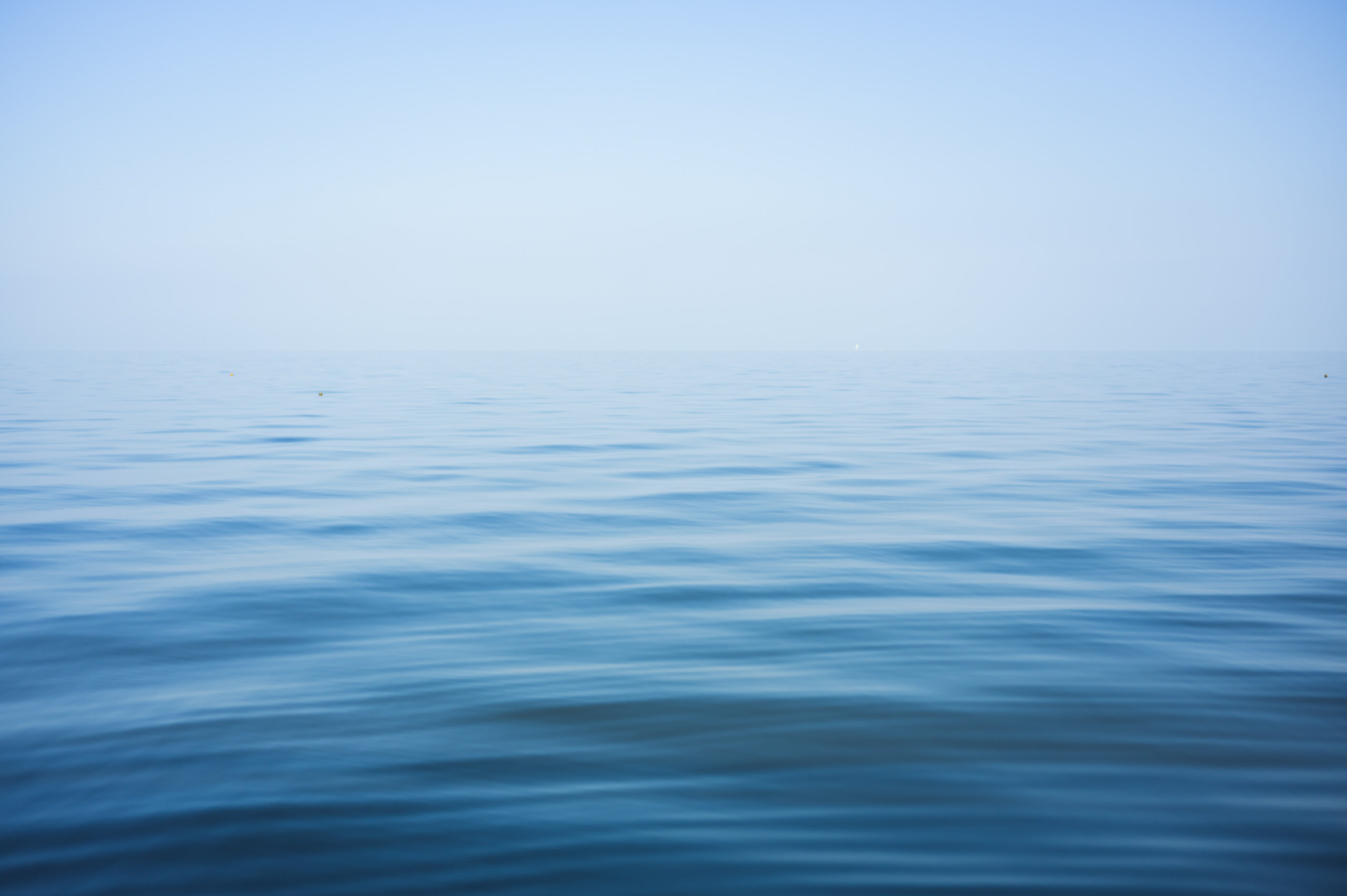 A calm, blue ocean stretches to the horizon under a clear sky, with gentle ripples on the water's surface.