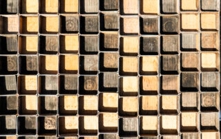 Stacked rectangular metal tubes filled with wooden blocks arranged vertically, creating a repetitive geometric pattern.